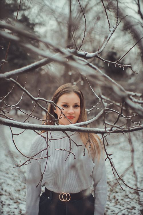 Free A woman standing in a snowy forest, with snow-covered branches in the foreground and a calm expression. Stock Photo