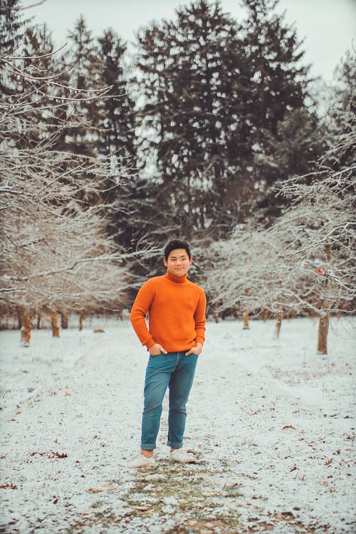 Man in Orange Sweater And Blue Denim Pants Standing Behind Tree Branch