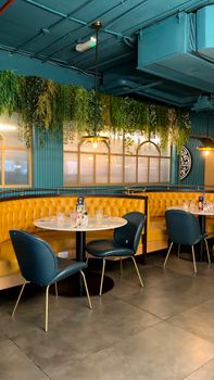 Chic restaurant interior featuring yellow booths and blue chairs, under hanging greenery.
