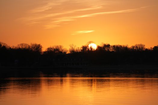 A tranquil sunset over a lake with vivid orange hues reflecting on the water.