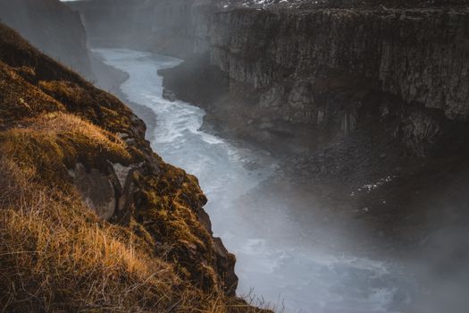 A breathtaking view of a river canyon in Iceland, showcasing mist and rugged terrain.