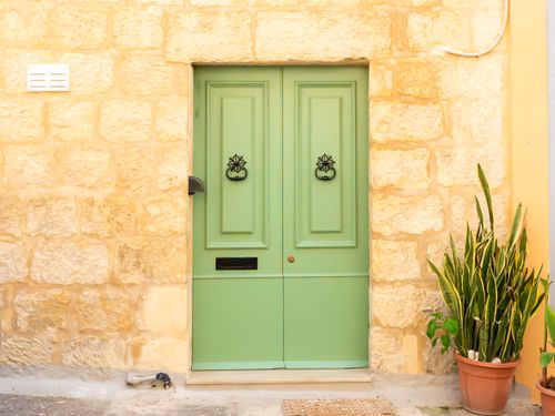 Free A vintage-style green door with traditional knockers against a rustic stone wall, complemented by a potted plant. Stock Photo