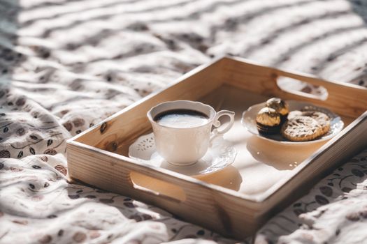 A cozy morning setup featuring a hot coffee cup and cookies on a wooden tray, perfect for breakfast in bed.