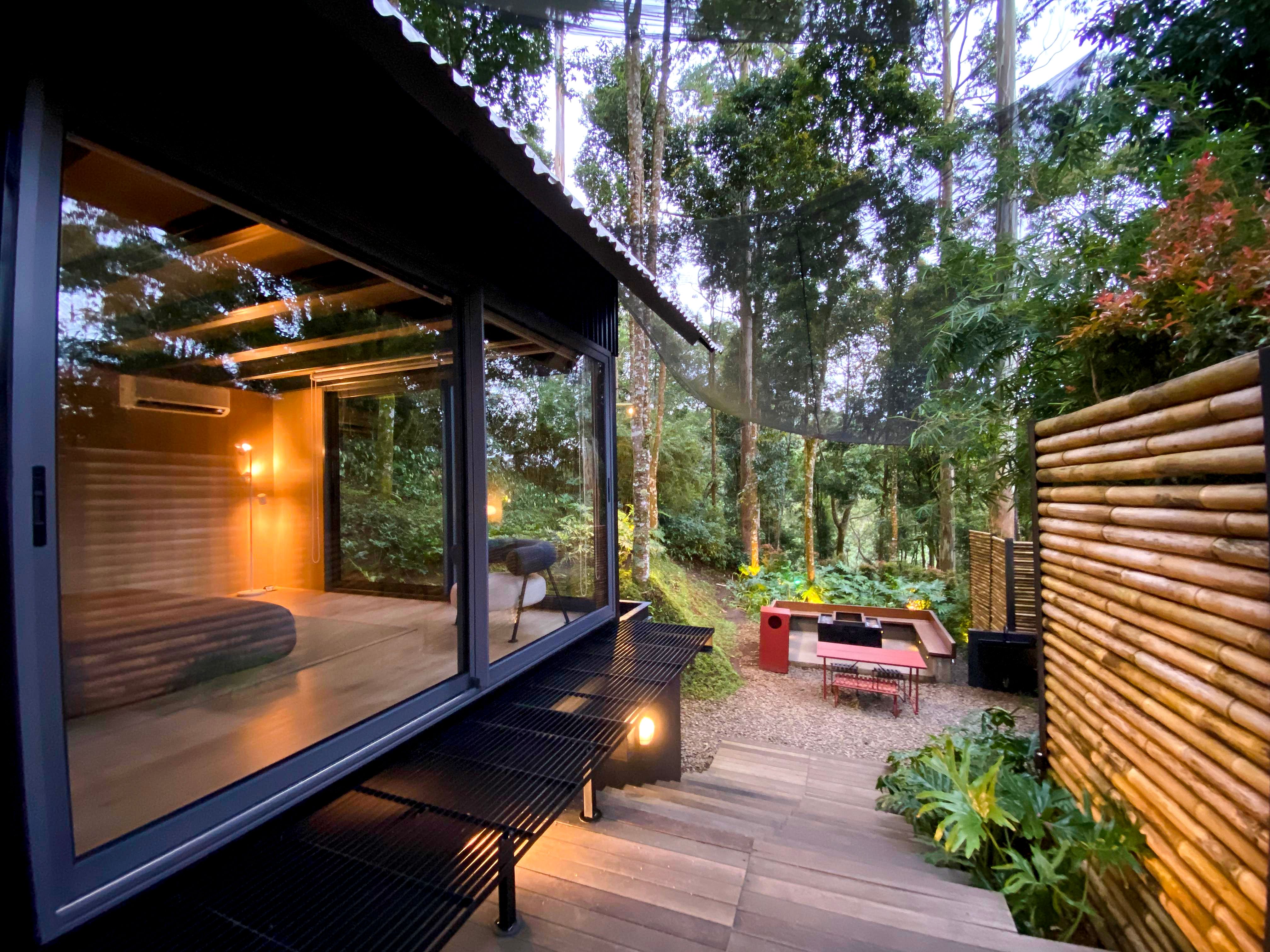 Studio de jardin vitré sur une terrasse en bois, palissade à lattes, éclairé le soir