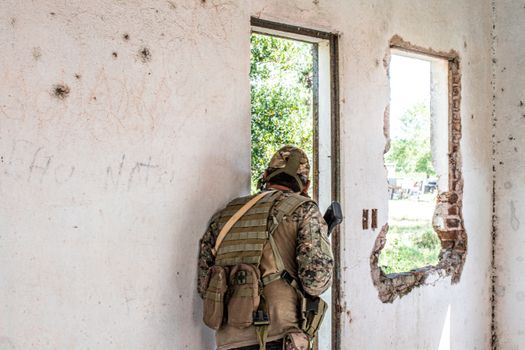 Airsoft player in camouflage navigating through a deserted, partially destroyed building.