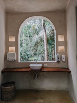 现代浴室设计配有一扇大窗户，窗外可见郁郁葱葱的绿色植物和棕榈树