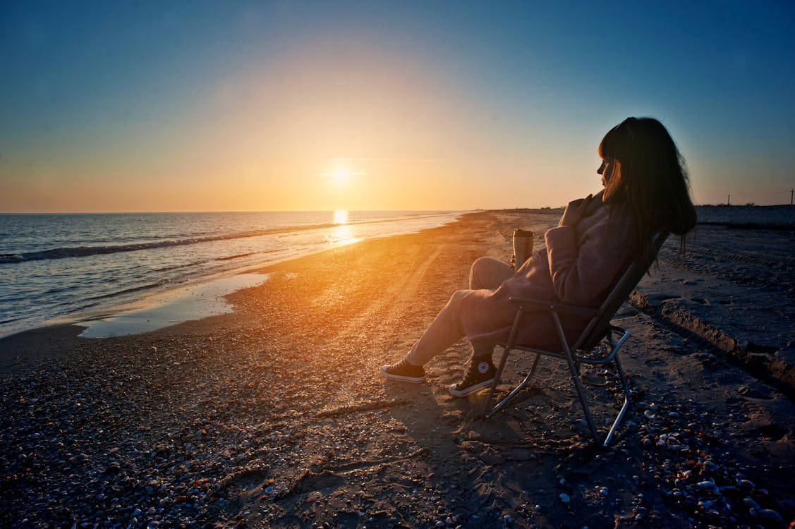 免費 女人坐在水邊旁邊的灰色鋼折疊扶手椅 圖庫相片