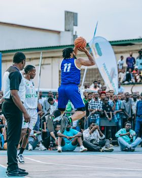 Basketball player in mid-air during a game, wearing blue jersey, outdoor court.