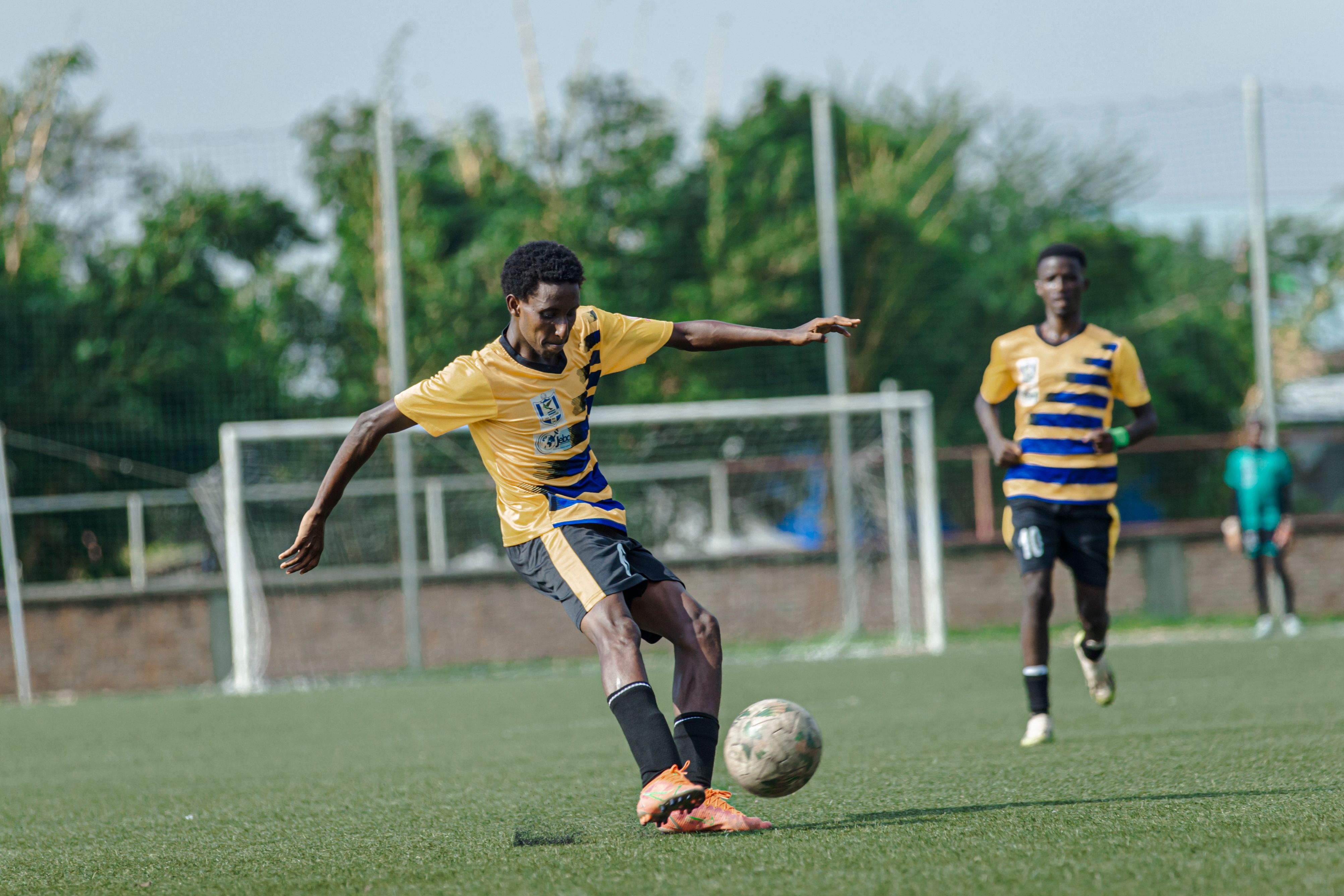Energetic action shot of a soccer player kicking the ball during a match on a sunny day.