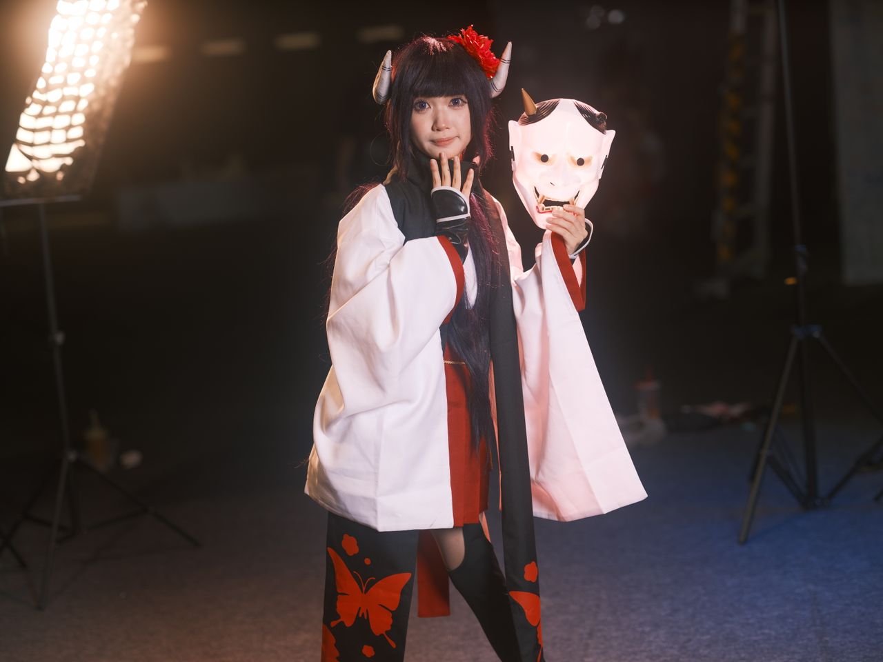 a cosplayer in traditional costume holding an oni mask during a photos