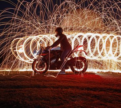 Dramatic motorcycle silhouette amid swirling steel wool sparks, creating a captivating night scene.
