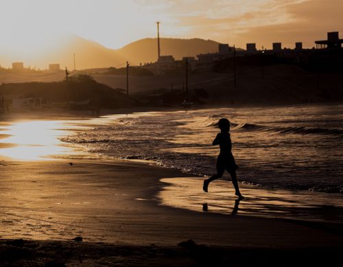 Free A child runs along a beach at sunset with cityscape and mountains in the background. Stock Photo