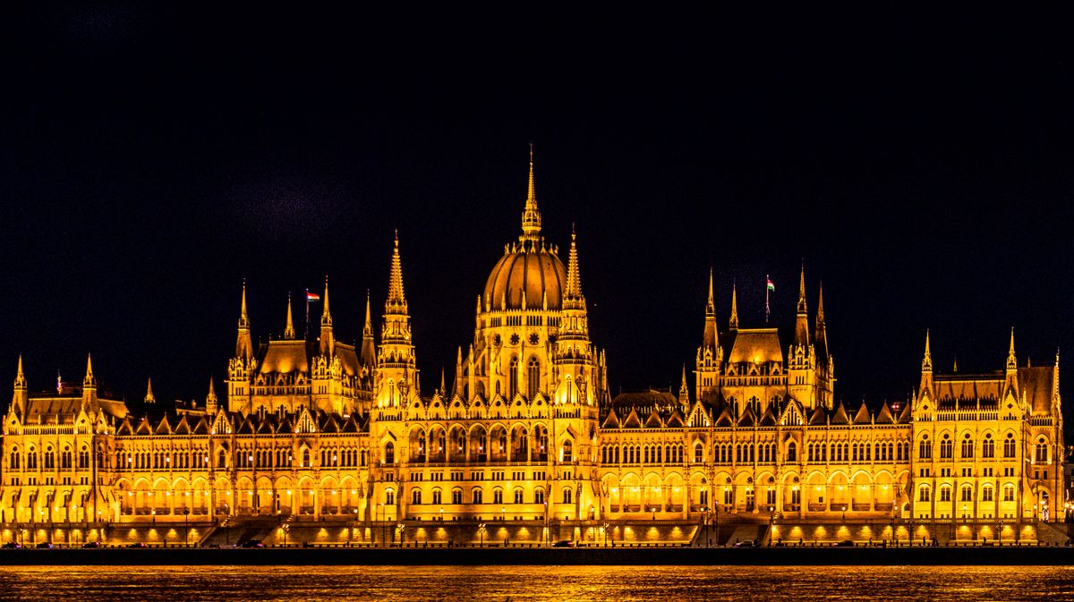 The Hungarian Parliament Building lit up in gold at night beside the Danube in Budapest