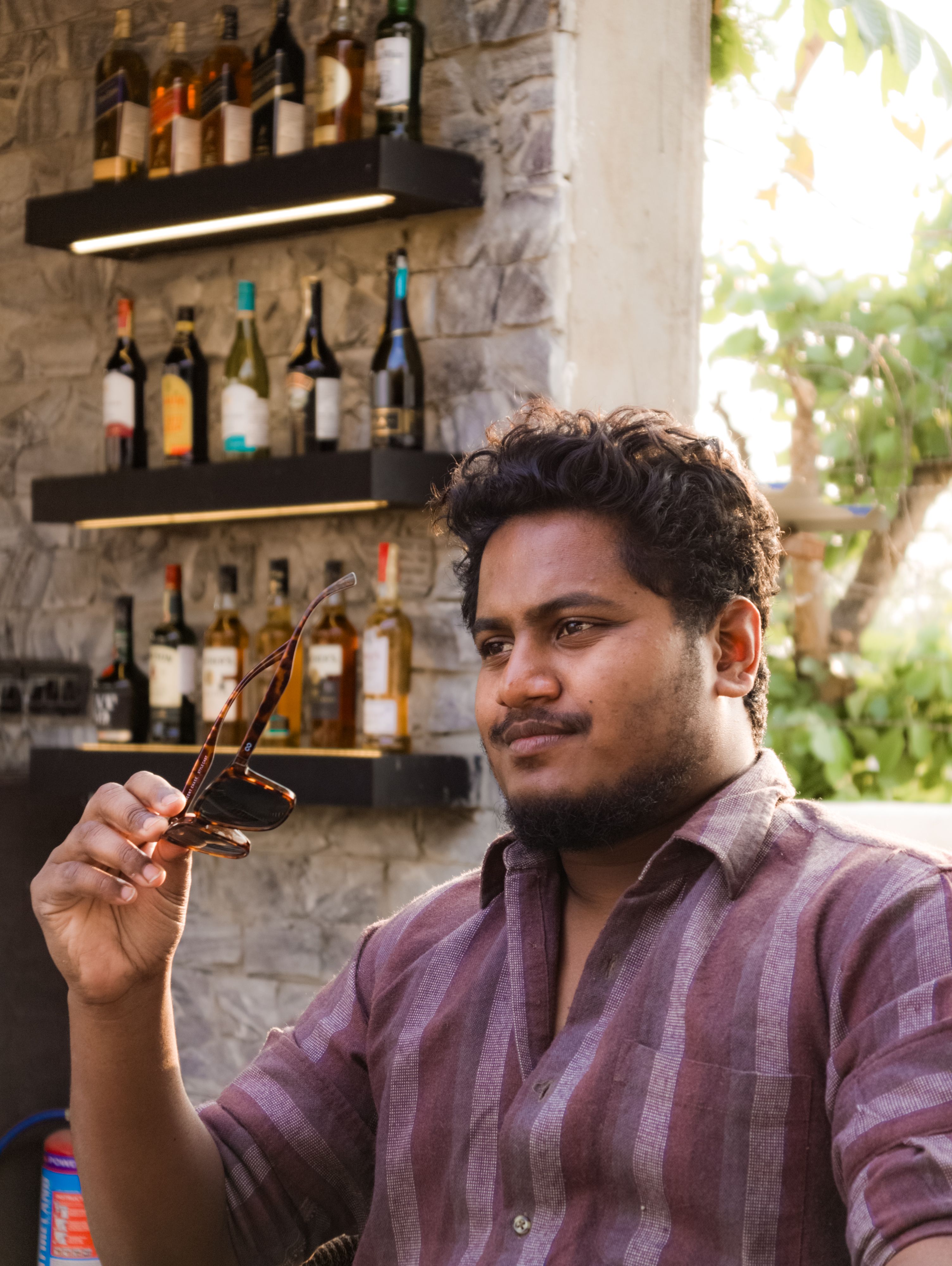Young man enjoying a relaxed moment with sunglasses at an outdoor bar.