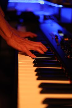 Close-up of hands playing a digital piano in a dimly lit room, focus on keys and fingers.
