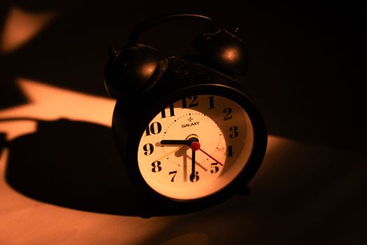 Old-fashioned black alarm clock casting a dramatic shadow under warm lighting.