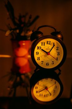 A vintage alarm clock with a classic design, beautifully reflected and warmly lit indoors.
