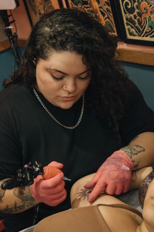 Free A skilled tattoo artist concentrates on tattooing a client's arm inside a studio with detailed wall art. Stock Photo