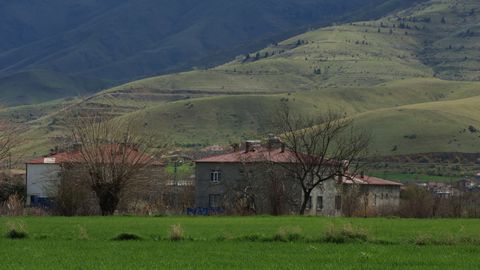 Idyllic rural scene with houses set against a backdrop of rolling green hills.