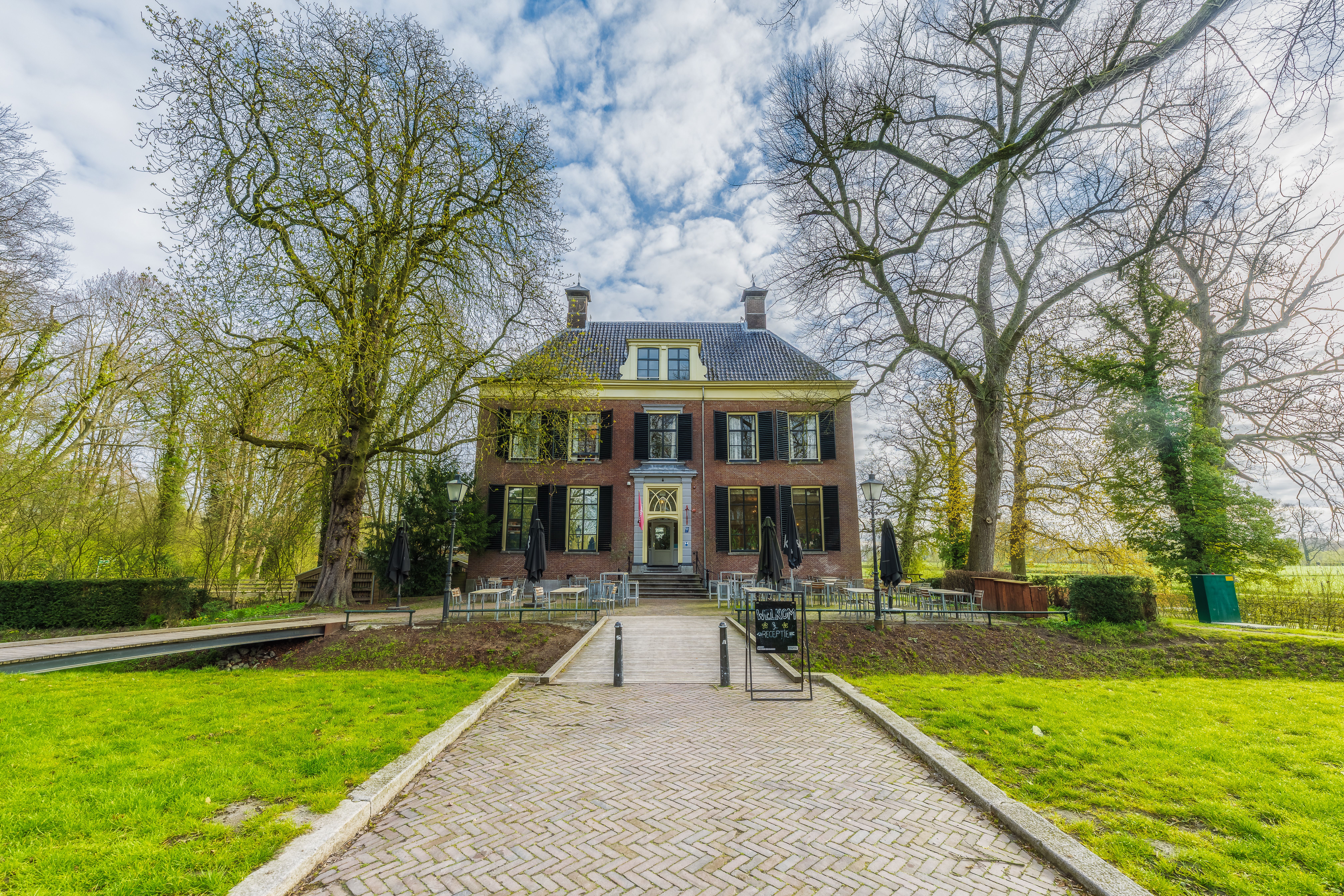 Elegant historical mansion surrounded by lush greenery and outdoor seating, under a vibrant spring sky.