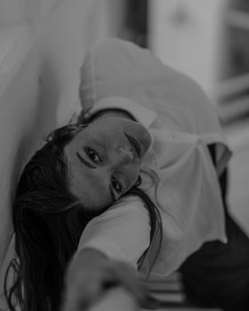 Moody black and white portrait of a woman leaning against a wall, creating a dramatic pose.