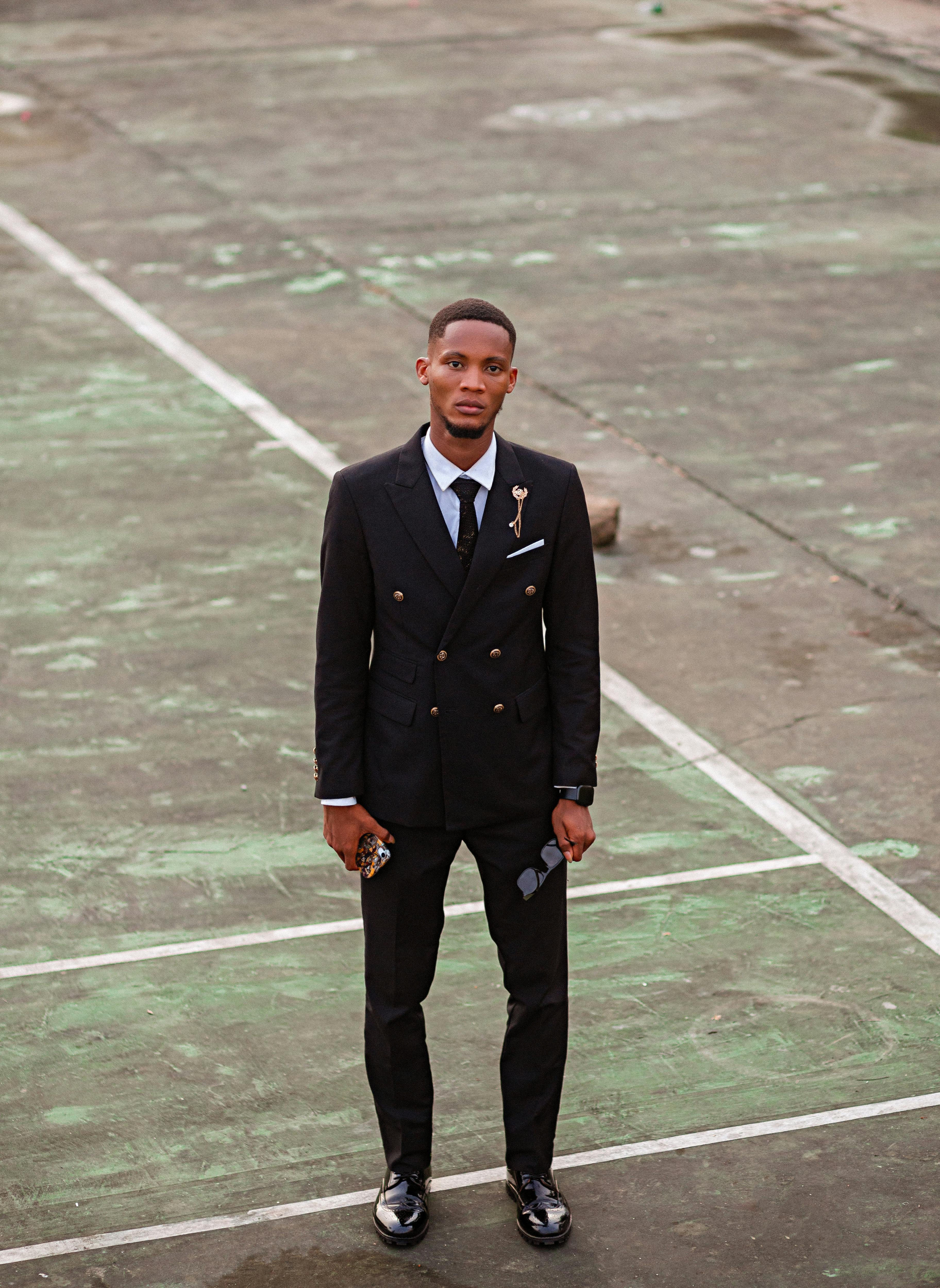 Stylish man in a black suit stands on an outdoor court, epitomizing modern fashion.