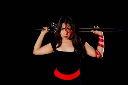 Free Fierce female warrior in cosplay with sword and face paint, poised against a black background. Stock Photo