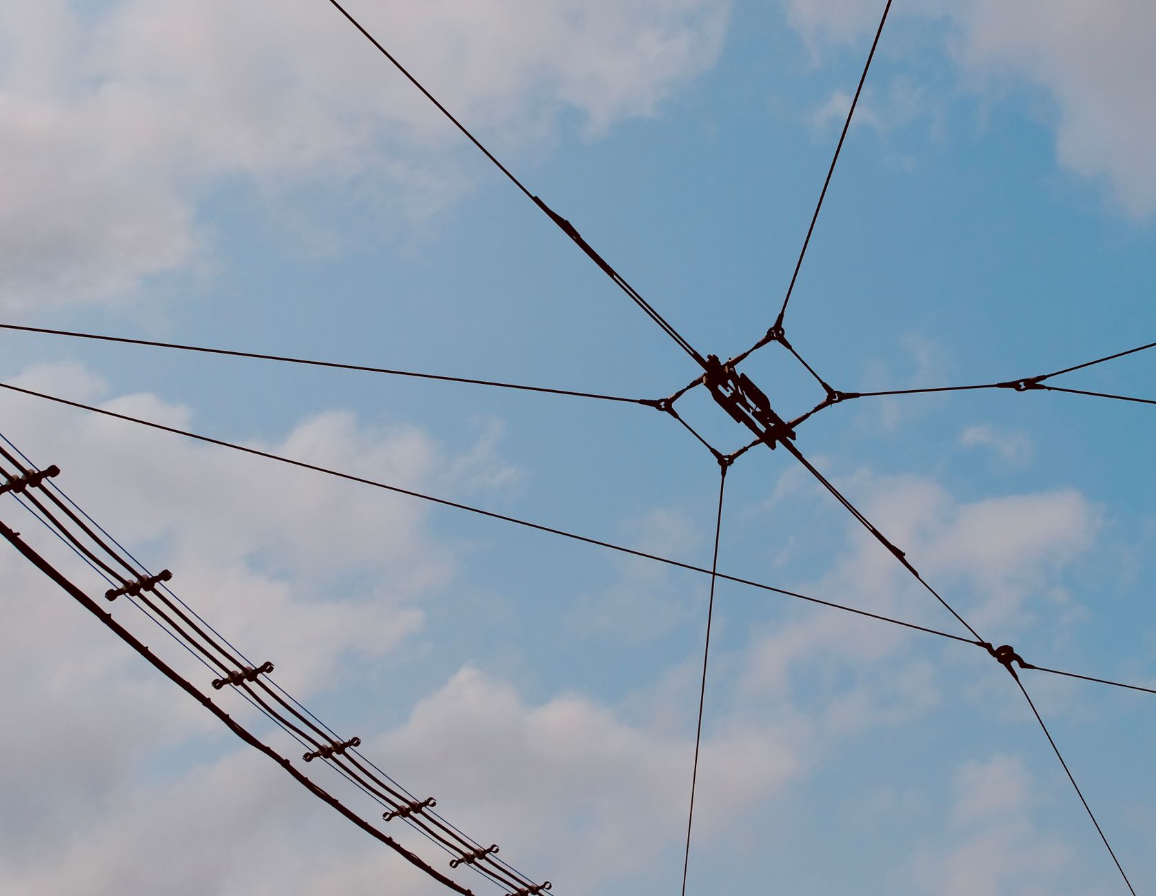 A network of power lines stretching across a blue sky with clouds.
