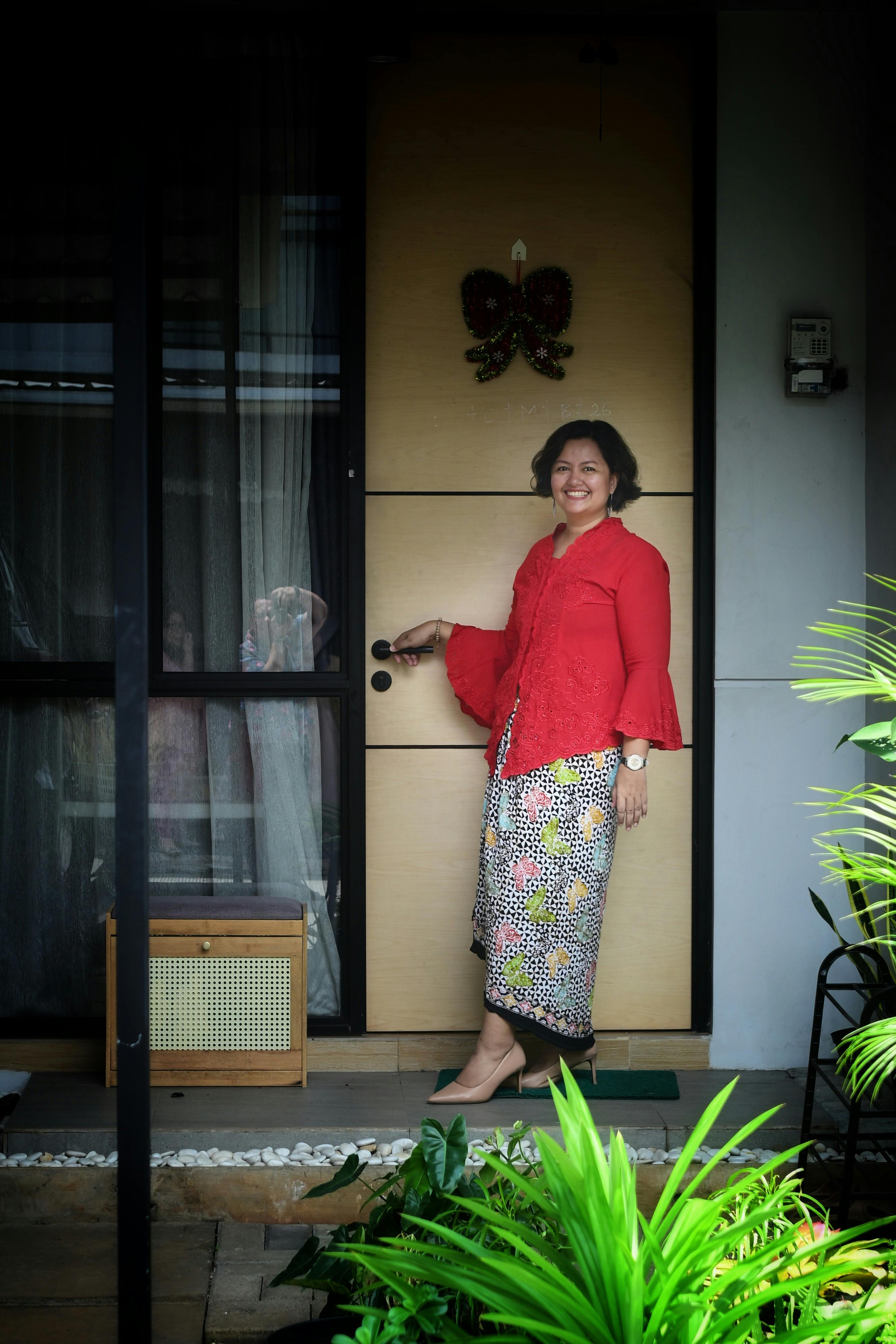 A cheerful woman stands at a home's entrance, ready to greet guests.