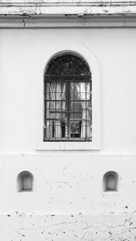 A monochrome image of an arched window on a weathered building facade.