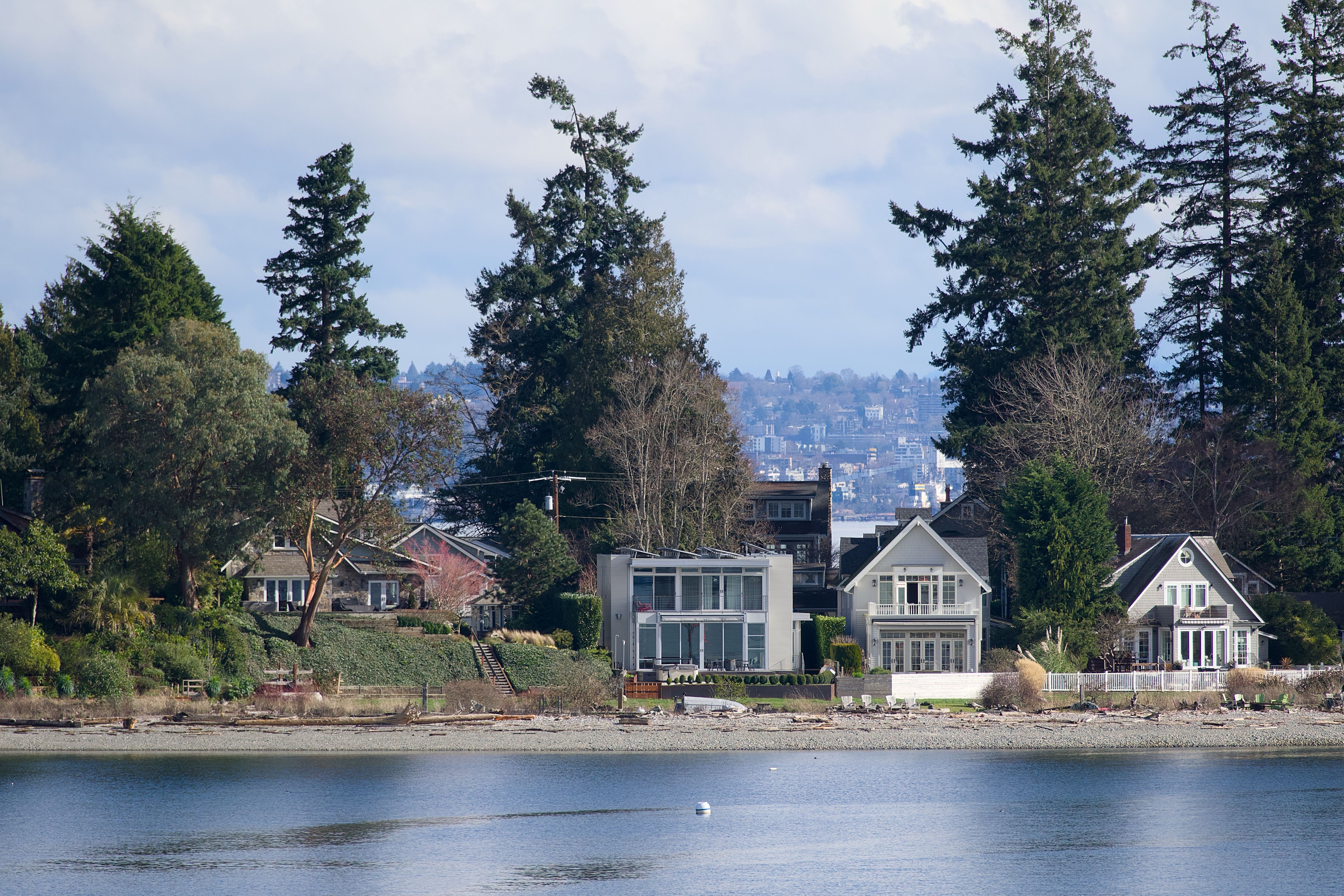 Charming waterfront homes along Bainbridge Island's beach, with lush trees and tranquil waters.