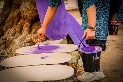 Close-up of a person painting with purple paint in an outdoor setting, showcasing creative expression.