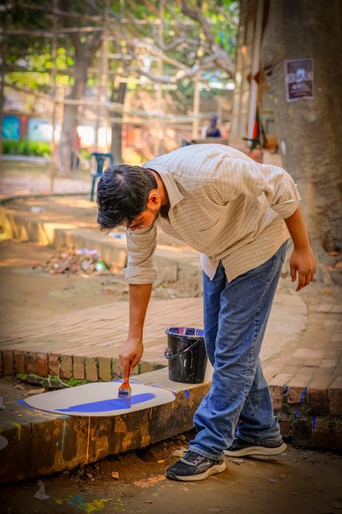 Free An adult man painting on a circular canvas outdoors in a park setting. Stock Photo