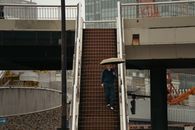 A man descends a staircase with an umbrella in Tokyo's urban architecture.