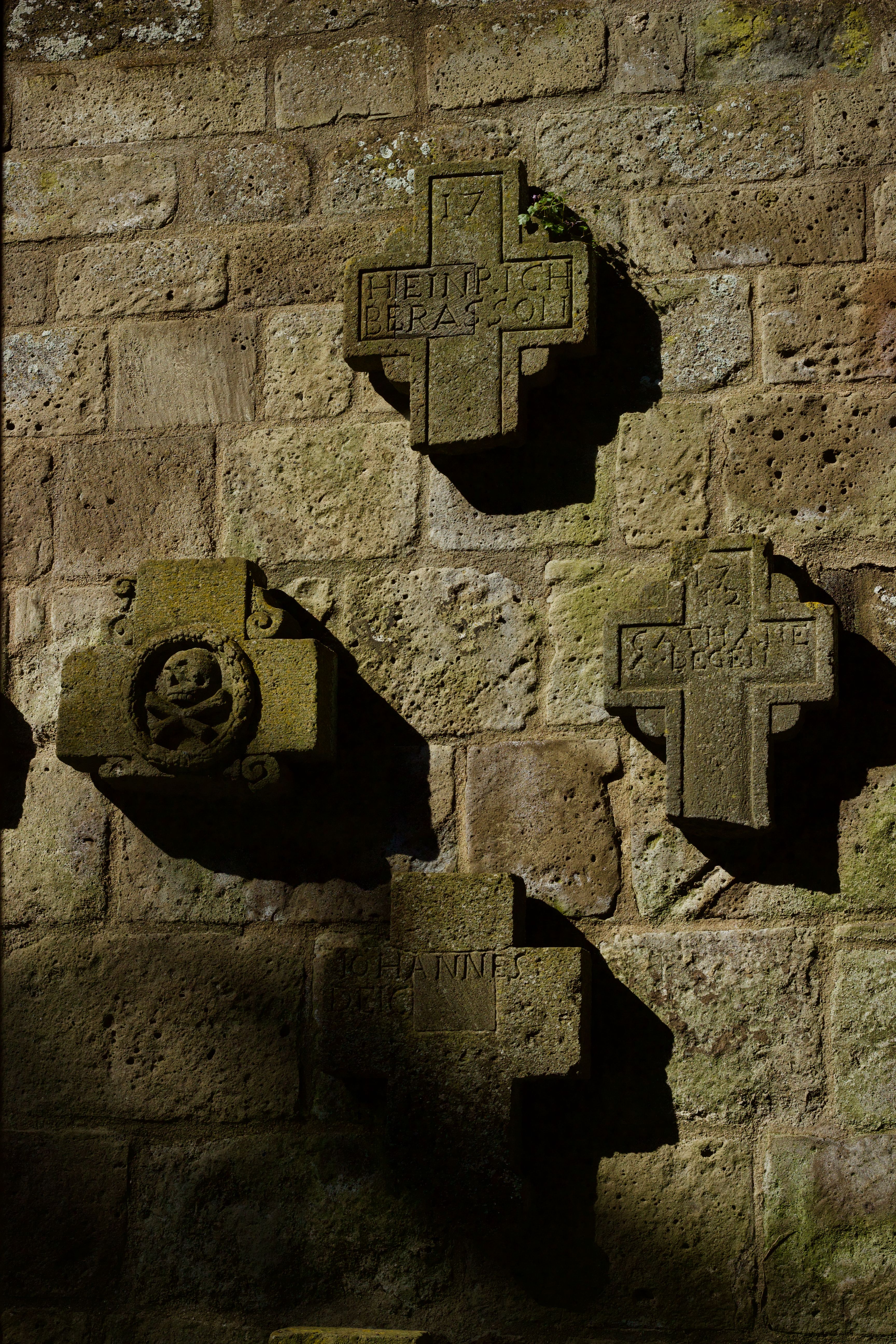 Weathered stone crosses casting shadows on an ancient brick wall, highlighting historical architecture.