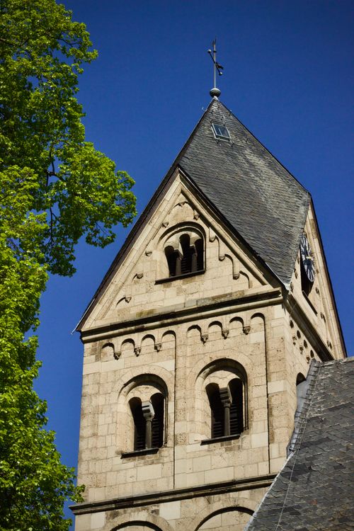 Free Close-up of a medieval stone church tower with a cross, set against a clear blue sky in summer. Stock Photo