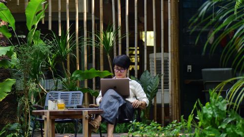 Free Woman working on a laptop in a serene garden setting surrounded by lush greenery. Stock Photo