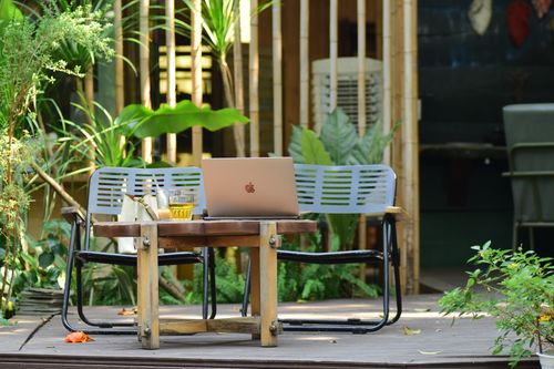 Free A serene outdoor workspace featuring a laptop and tea on a wooden table surrounded by lush greenery. Stock Photo