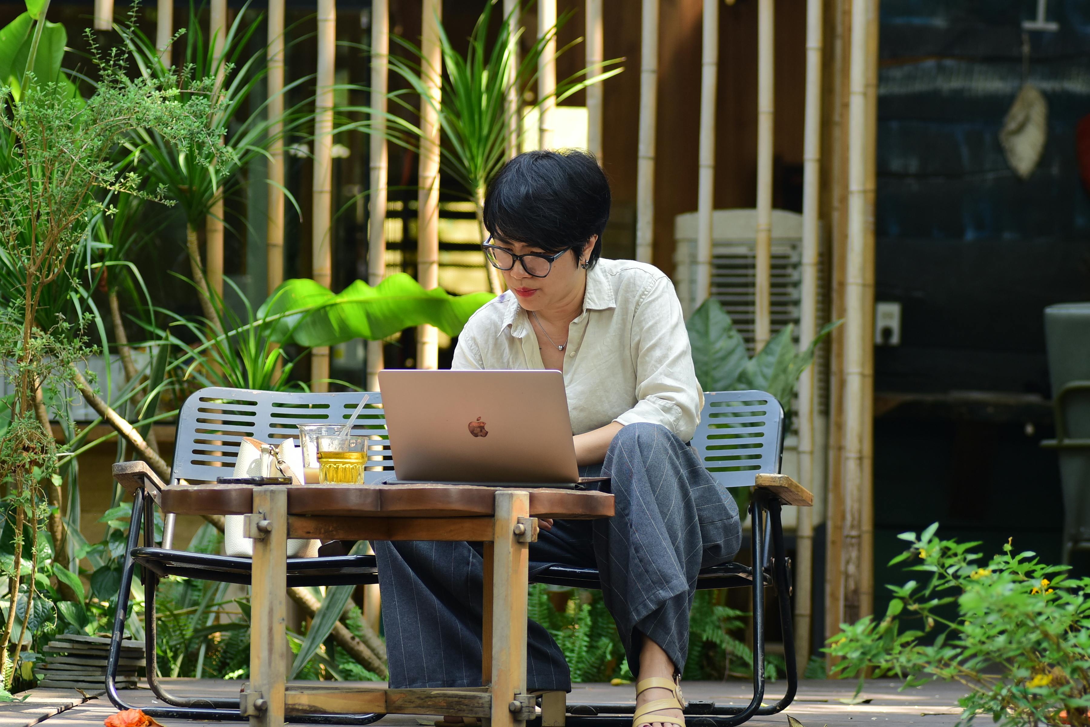 Woman working on a laptop in a lush outdoor café setting.