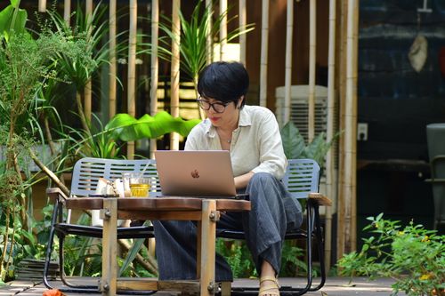 Free Woman working on a laptop in a lush outdoor café setting. Stock Photo