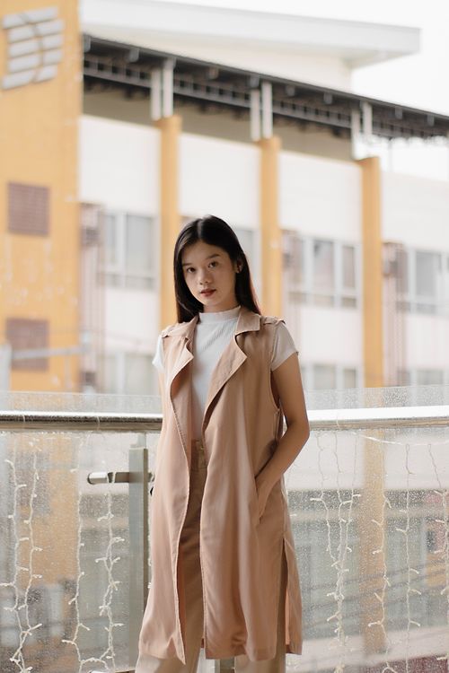 Free A young woman in casual wear poses on a balcony, with a city building in the background. Stock Photo