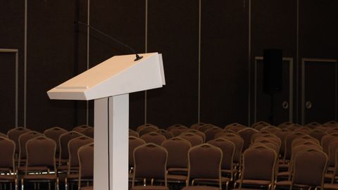 An empty conference room setup with podium and rows of chairs, ready for an event.