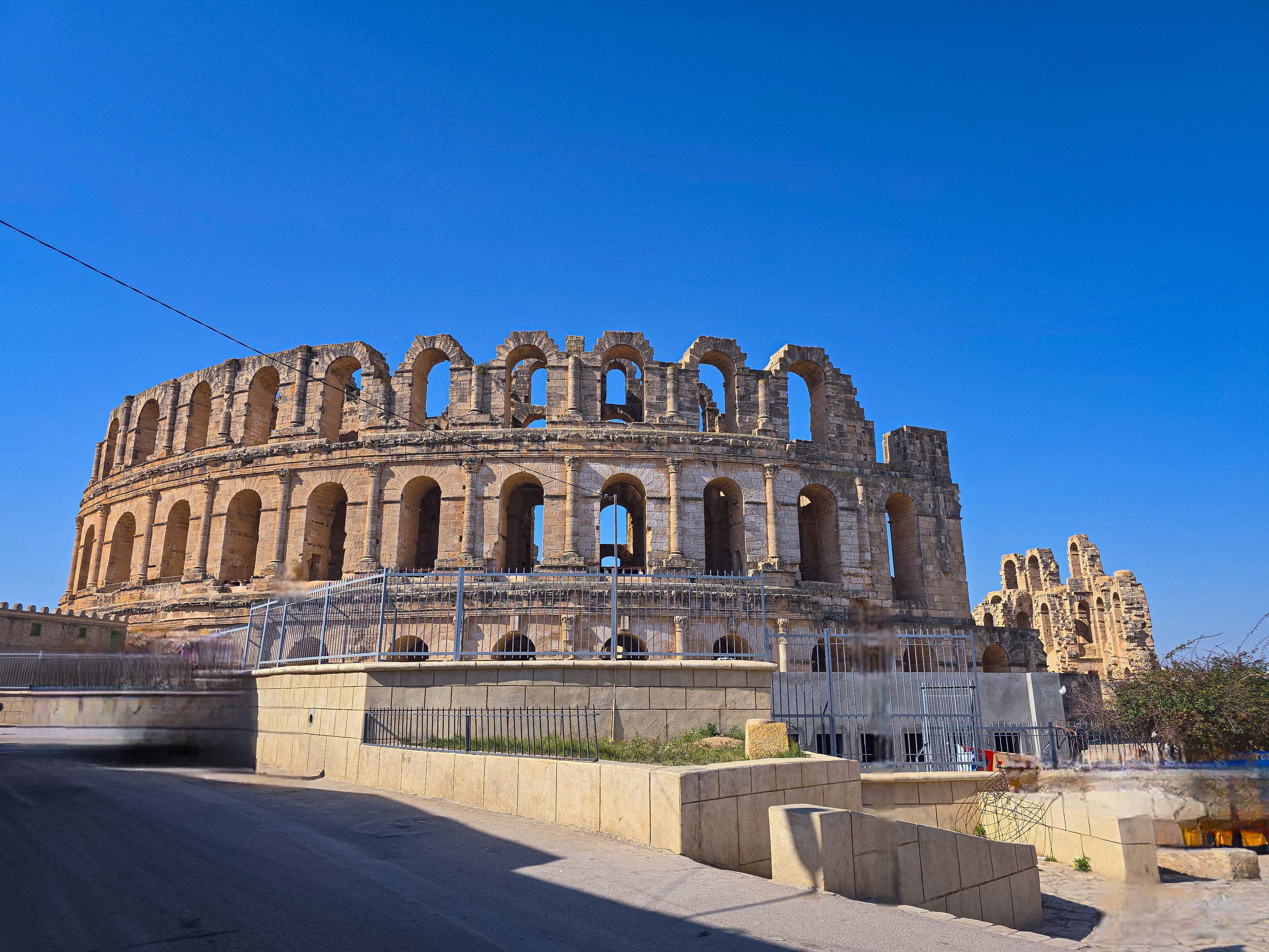 Stunning daytime view of the ancient Roman Amphitheater in El Jem, Tunisia under a clear blue sky.