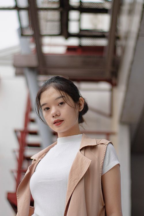 Free Low angle of graceful young Asian lady with long dark hair in stylish outfit standing n street near building with metal stairs and looking at camera Stock Photo