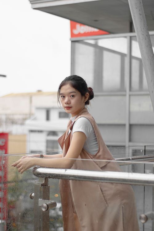 Free Side view of pensive young Asian female with dark hair in stylish outfit leaning on metal railing while standing on terrace of modern building and looking at camera Stock Photo