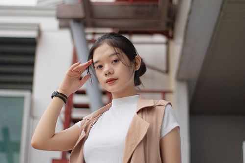Free From below of confident young ethnic lady touching dark hair and looking at camera while standing near building on street Stock Photo