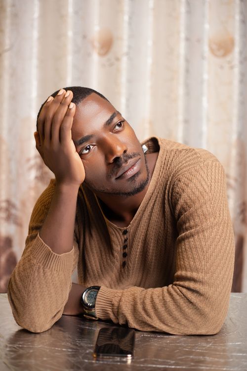 Free Thoughtful young man sitting indoors, resting his head on his hand, deep in contemplation. Stock Photo