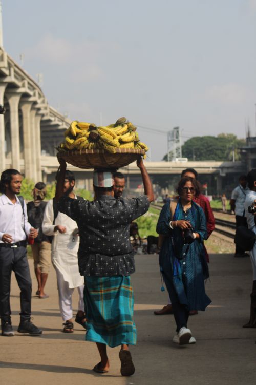 Free Street vendor carries a basket of bananas on head at bustling train station. Stock Photo