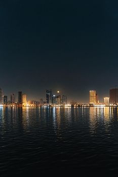 Stunning cityscape at night with skyline reflections on water in a vibrant urban setting.