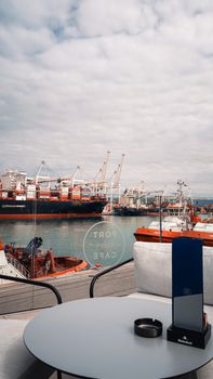 Enjoy a scenic view of a bustling port with ships and cranes from a modern cafe setting.